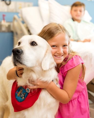 Young girl with beaming smile hugging a golden retriever therapy dog