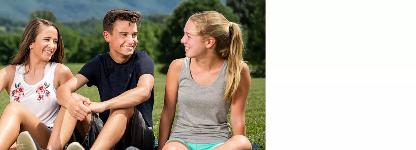 Two young women and a young man sitting in a field