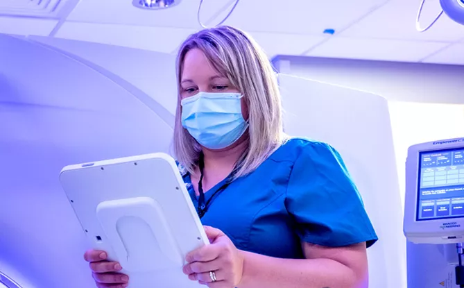 Woman wearing scrubs and medical mask reading results from a digital screen
