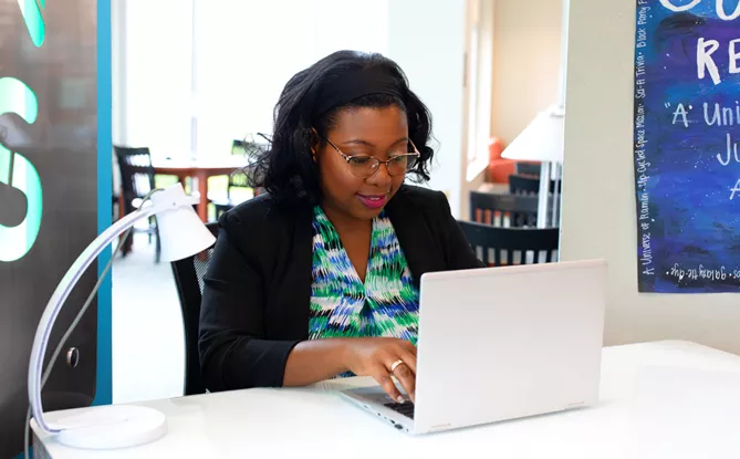 Woman wearing business casual sitting at a desk, typing on her laptop