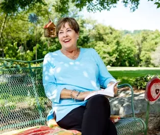 Shelia Minier sitting on a park bench, smiling and reading a book
