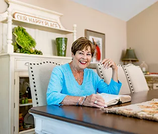 Shelia smiling over an open book while sitting at a kitchen table