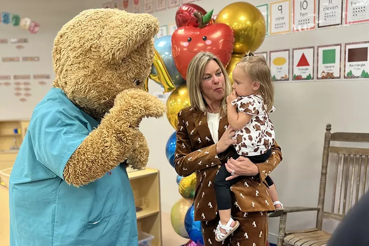 Photo of Ballad Health's mascot, Scrubs, with a woman holding a toddler