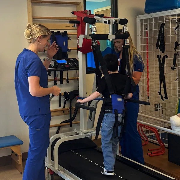 Physical therapists and a pediatric patient using a treadmill