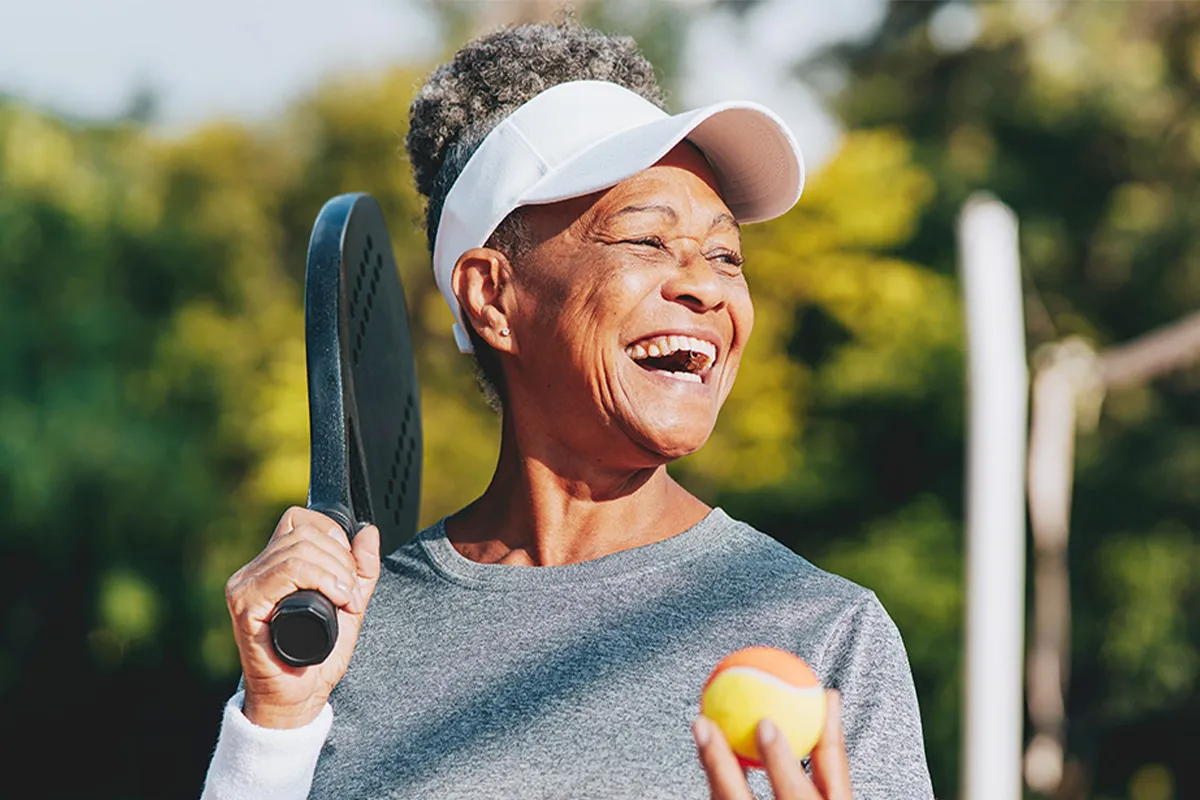 Elderly woman smiling and holding a pickle ball and paddle