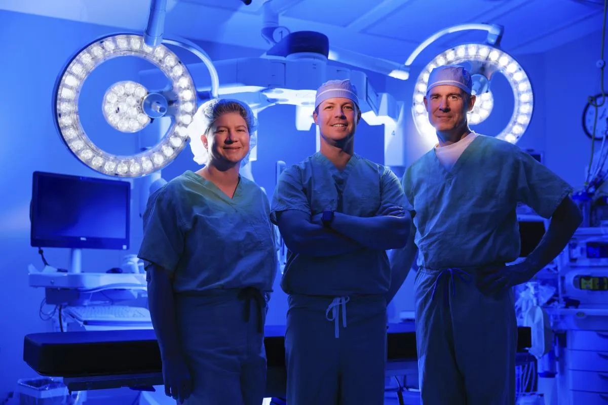 Three robotic surgeons standing in front of the da Vinci robotics system